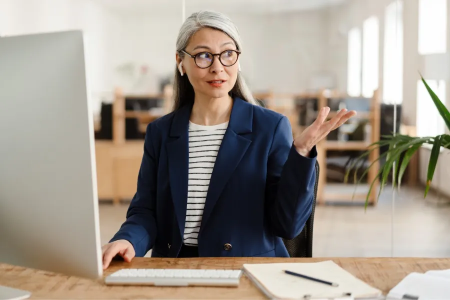 Woman with grey hair speaking at desk, showing facial expression and natural features