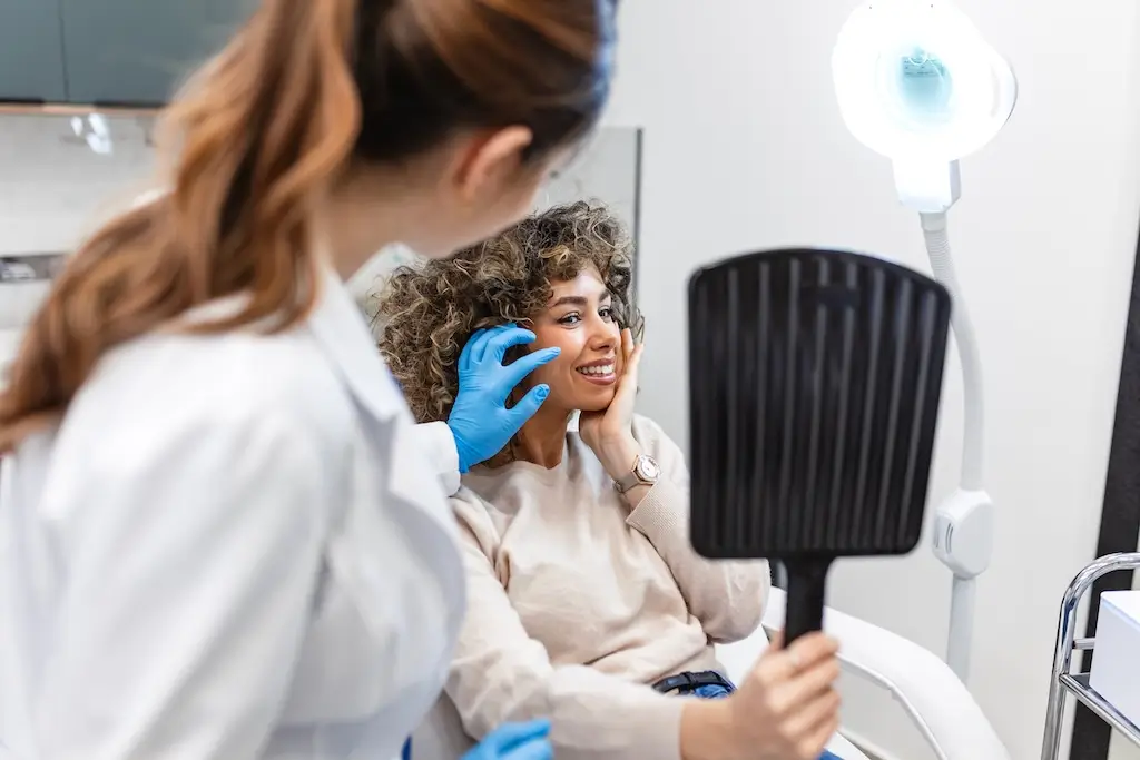 Clinician discussing cosmetic treatment for face after weight loss with smiling patient holding a mirror