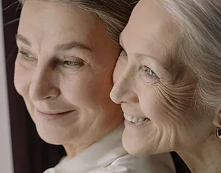 Two older women smiling and looking into the distance, heads close together