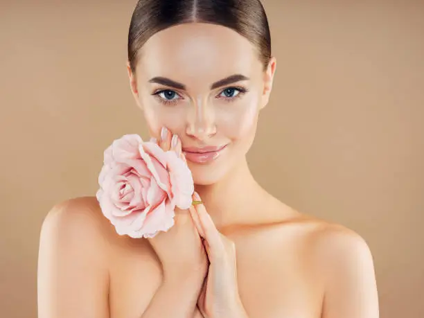 Woman with smooth skin and defined facial features holding a pink rose against her cheek, illustrating a balanced and refined face shape.