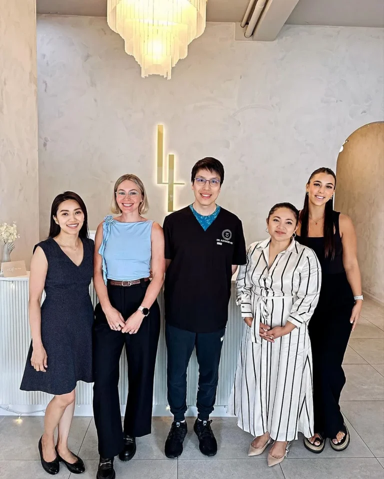 Six members of the Luxe Lips team standing together in the clinic reception beneath a chandelier