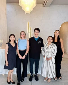 Six members of the Luxe Lips team standing together in the clinic reception beneath a chandelier
