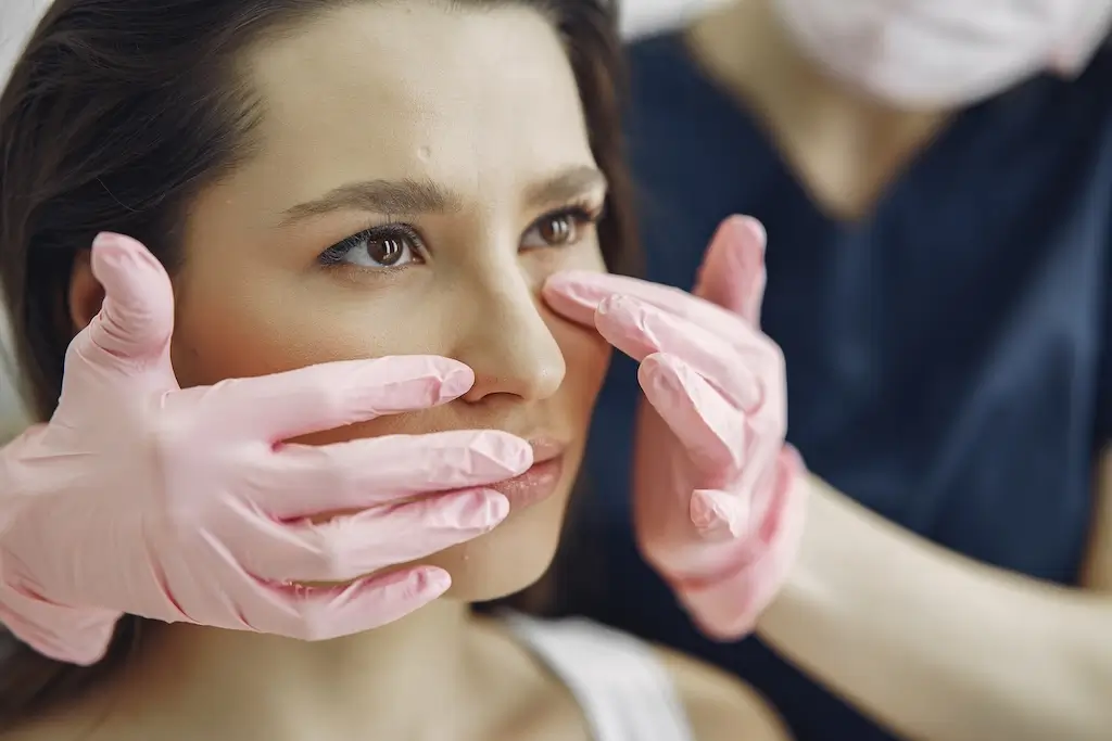 Clinician gently examines a woman’s nose during a nose thread lift procedure consultation.