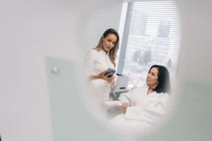 Clinician shows a treatment plan on her phone while reviewing the patient&rsquo;s aesthetic maintenance schedule in clinic