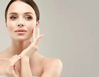 A woman gently touching her face and hands to showcase smooth results after following proper hand filler aftercare.