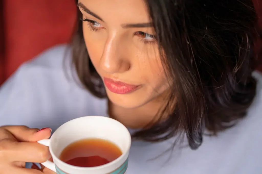 A close-up shot of a woman with red lipstick holding a mug of dark liquid, illustrating the need to avoid hot drinks in the first 24 hours after lip enhancement.