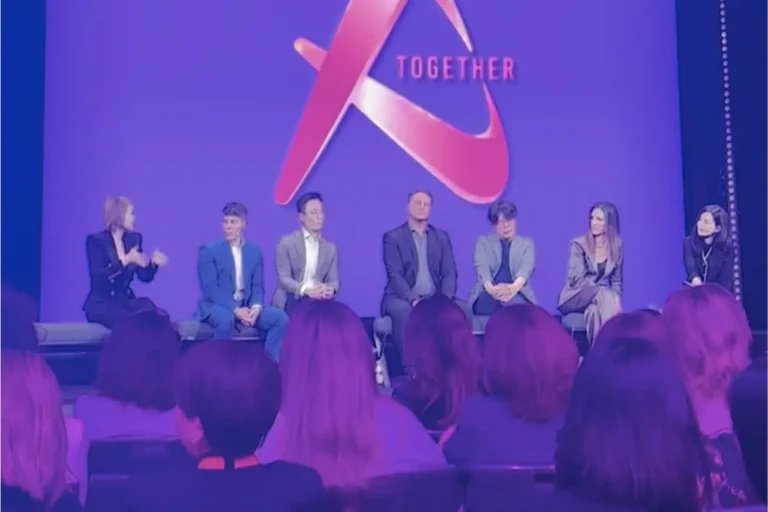 Panel of seven speakers seated on stage at an aesthetics industry conference, with an audience in the foreground