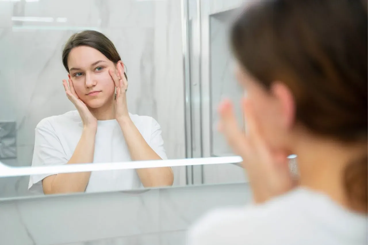 Woman examining her skin in the mirror while considering if she is a candidate for a facial thread lift