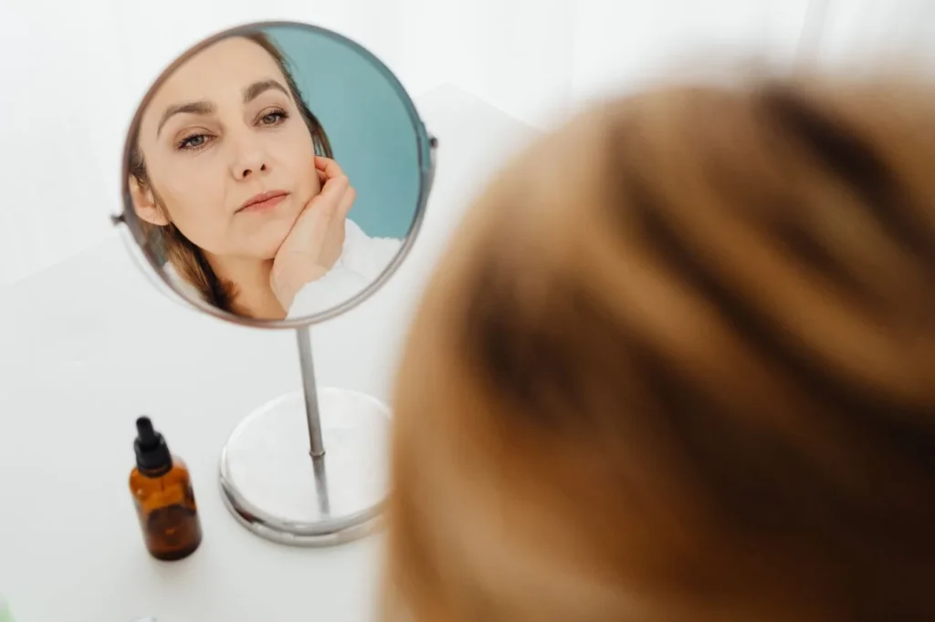Woman looking at her clear skin in a mirror, considering how long Lumecca results last