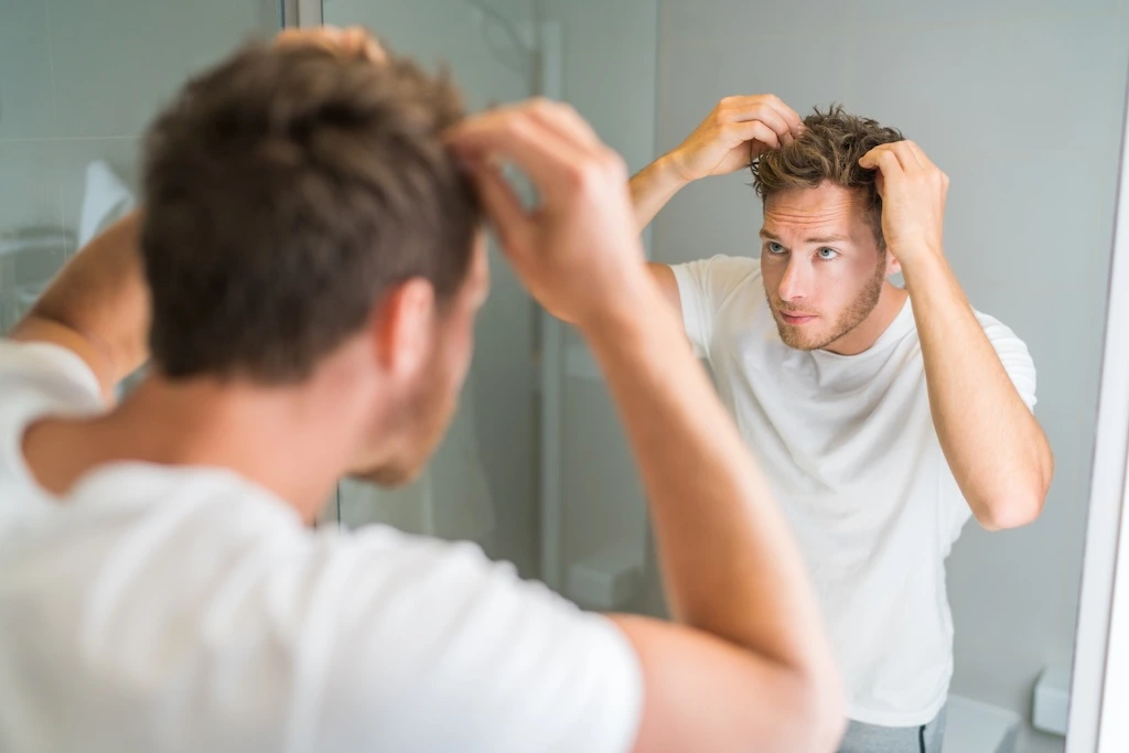 Man checking his hairline in the mirror, looking at what causes hair loss in men